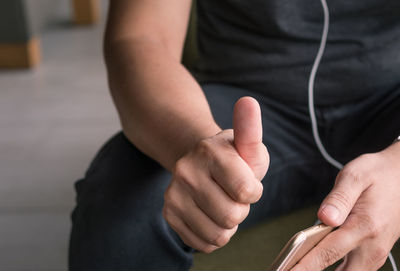 Midsection of man with phone showing thumbs up