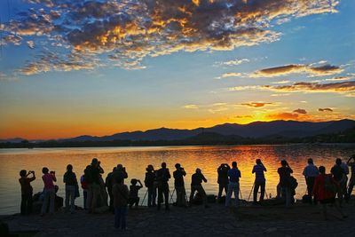 People standing on beach against sky during sunset