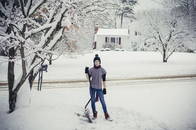 Portrait of teenage boy removing snow with shovel at yard