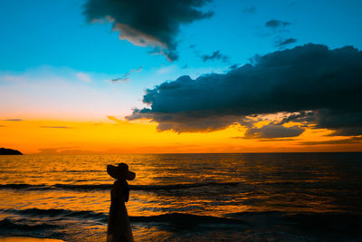 Silhouette person standing by sea against sky during sunset