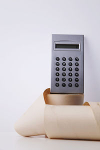 Close-up of calculator and paper roll on table against white background