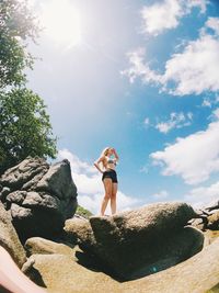 Low angle view of young woman standing on rock against sky