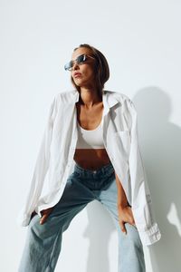 Young woman wearing sunglasses while standing against white background