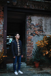 Young man looking away while standing against brick wall