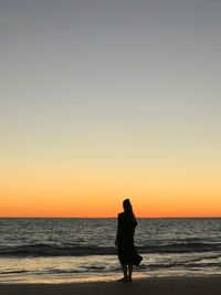 Silhouette woman on beach against sky during sunset