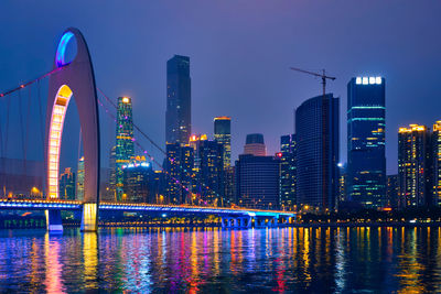 Illuminated buildings by river against sky at night