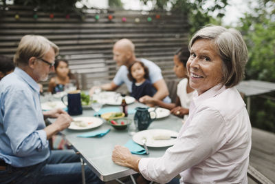 Portrait of happy senior woman sitting with family at outdoor dining table