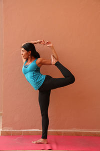 Full length of woman performing yoga while standing against orange wall