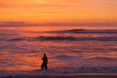 Silhouette of amateur fisherman in the sunset, sport fishing, recreational fishing on the beach