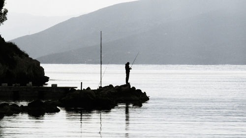 Silhouette fishing rod on rock by sea against sky