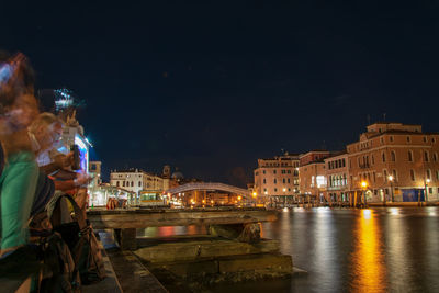 Illuminated city by river against sky at night