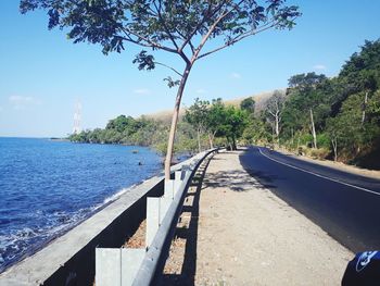 Road by sea against sky on sunny day