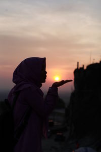 Side view of silhouette man holding orange against sky during sunset