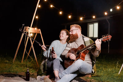 Woman recording with phone by man playing guitar at night