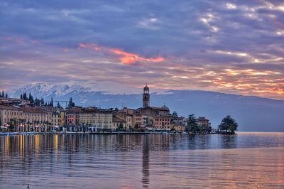 Town and mountains by lake garda against cloudy sky