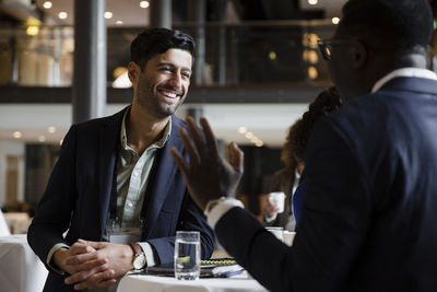 Happy businessman leaning on table while talking with entrepreneur at seminar