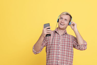 Young man using smart phone against yellow background