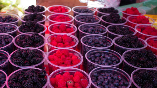 Raspberries, blackberries and blueberries in transparent plastic containers on a market stand