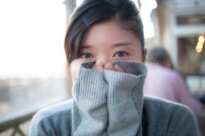 Close-up portrait of young woman covering face with hands at cafe