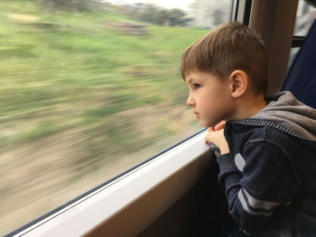 Side view of boy looking through window of train