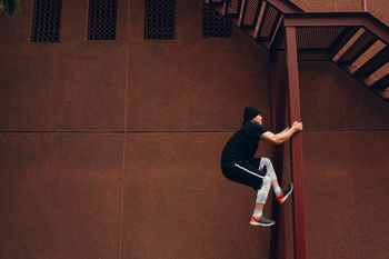 Man climbing on metal column against brown wall