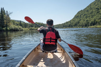 Rear view of man standing on boat in lake against clear sky