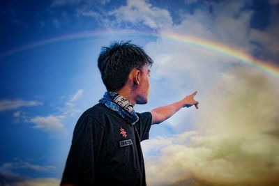 Low angle view of man standing against rainbow in sky