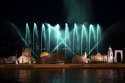 Illuminated fountain by building against sky at night