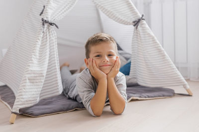 Cute baby is lying on his stomach in a tent-wigwam in the nursery in gray.