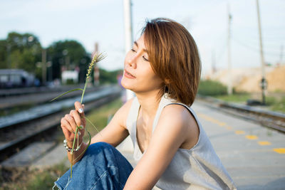 Woman holding plant while sitting against sky