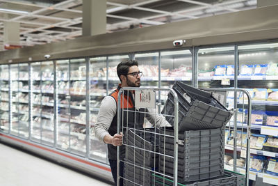 Sales clerk pushing cart with plastic crates at supermarket