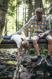 Father with apple holding daughter fishing on footbridge in forest