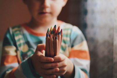 Midsection of boy holding colored pencils at home