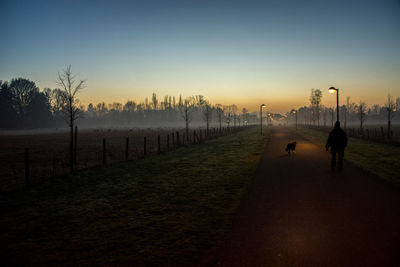 Silhouette man walking on footpath against sky during sunset