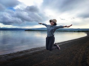 Full length of man with arms raised at beach against sky