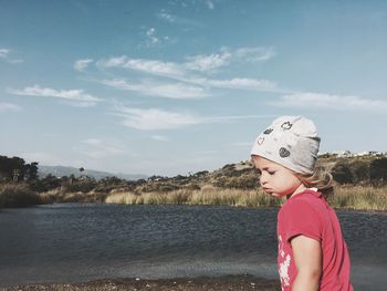 Side view of girl standing by lake against sky