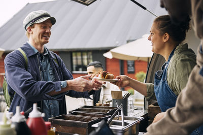 Young female owner serving hot dog to customer at food truck