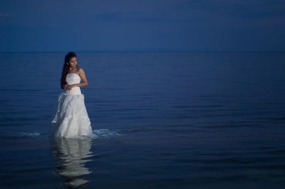 Woman wearing dress while standing in sea at night