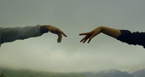 Cropped image of hands reaching each other against sky