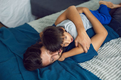 Bearded father hugs his baby boy lying on a bed in a white bedroom