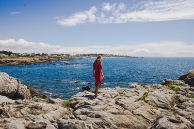 Teenage girl standing on rocky shore against sky