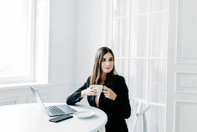 Young woman using mobile phone while sitting on table