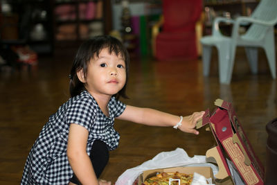 Portrait of cute girl opening boxes on floor at home