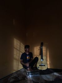 Young man playing guitar on table against wall at night