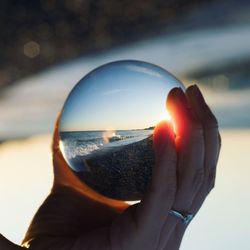 Close-up of hand holding crystal ball against sky