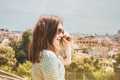 Profile portrait of young smiling woman in sunglasses with a panoramic view of rome, italy