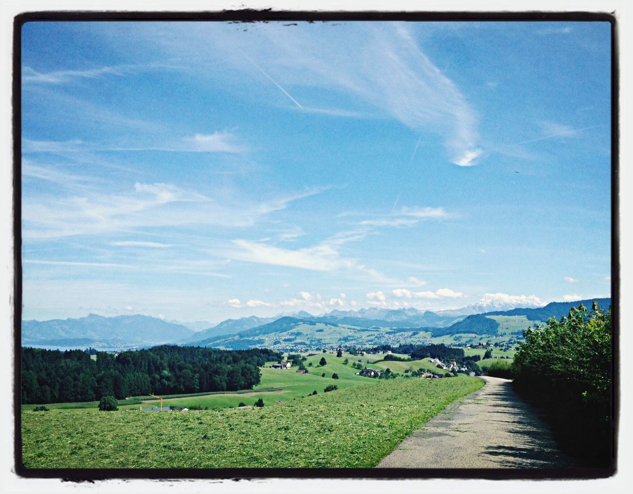 sky, transfer print, mountain, landscape, tranquil scene, grass, tranquility, scenics, blue, beauty in nature, auto post production filter, cloud - sky, nature, cloud, field, mountain range, road, building exterior, tree, rural scene