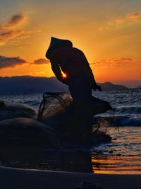 Silhouette man on rock at beach during sunset