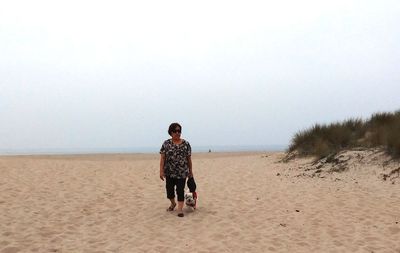 Woman with dog walking at beach against sky