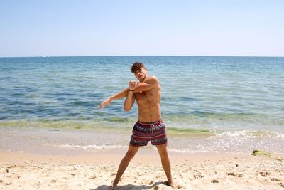 Full length of shirtless man standing at beach against sky